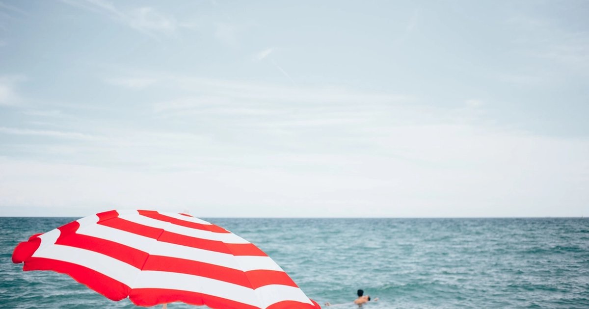A red and white striped beach umbrella with swimmers in the sea