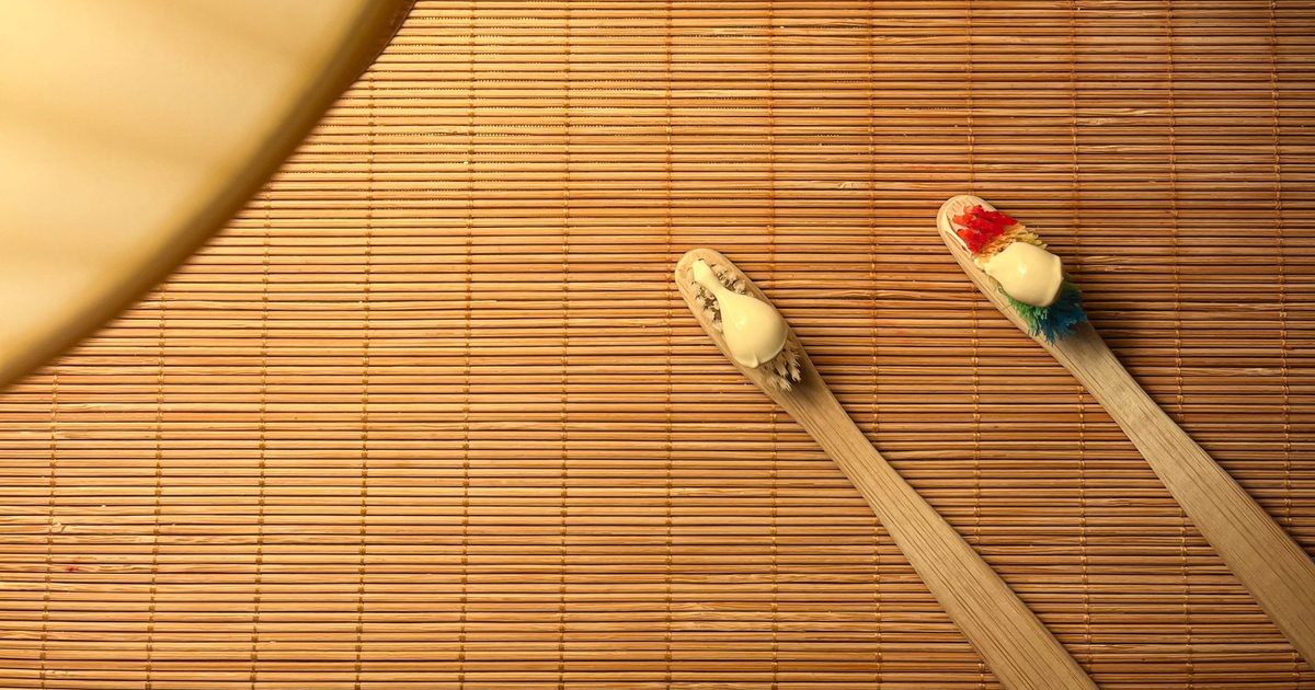 Two bamboo toothbrushes with toothpaste on a bamboo mat