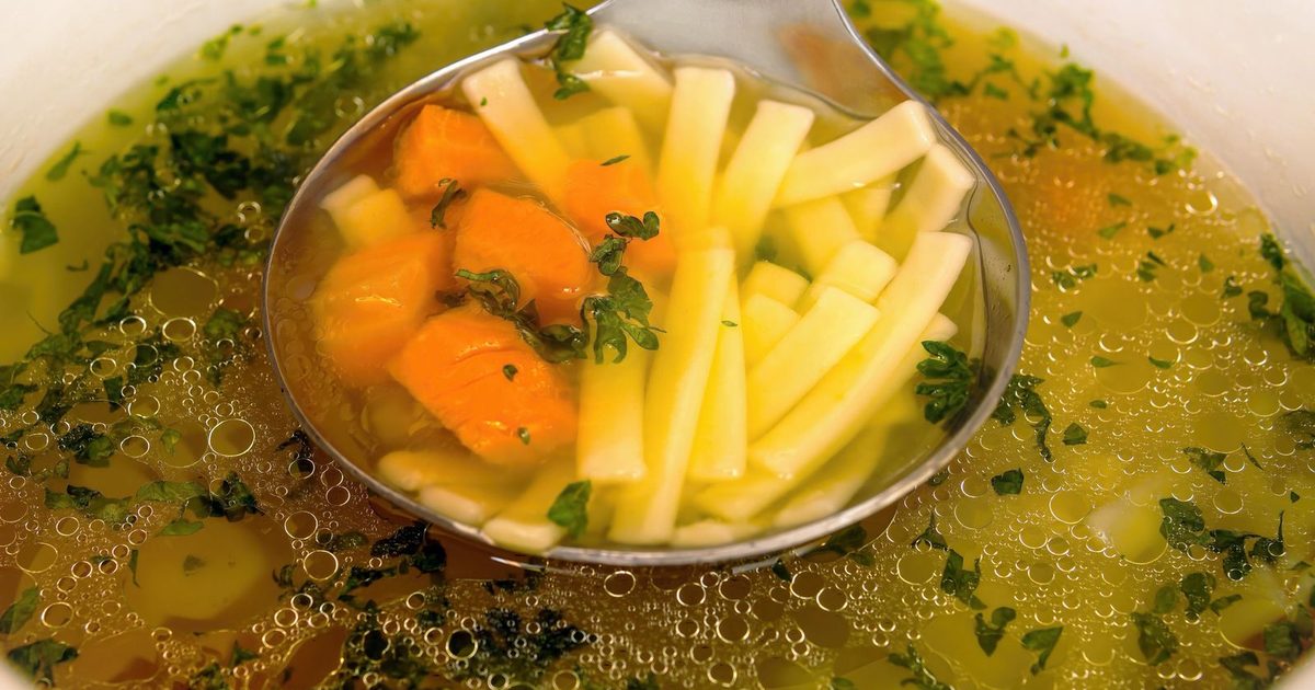 A spoonful of golden bone broth with carrot and fresh herbs lifted from a bowl
