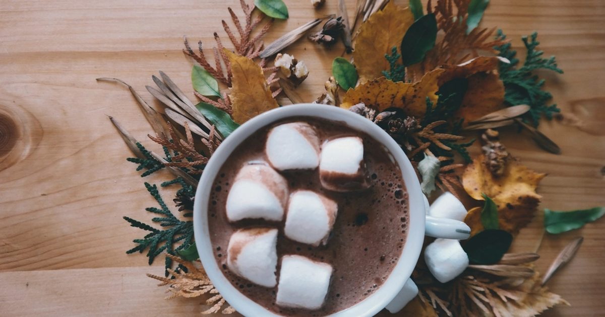 A mug of hot cacao topped with marshmallows on a wooden table among autumn leaves