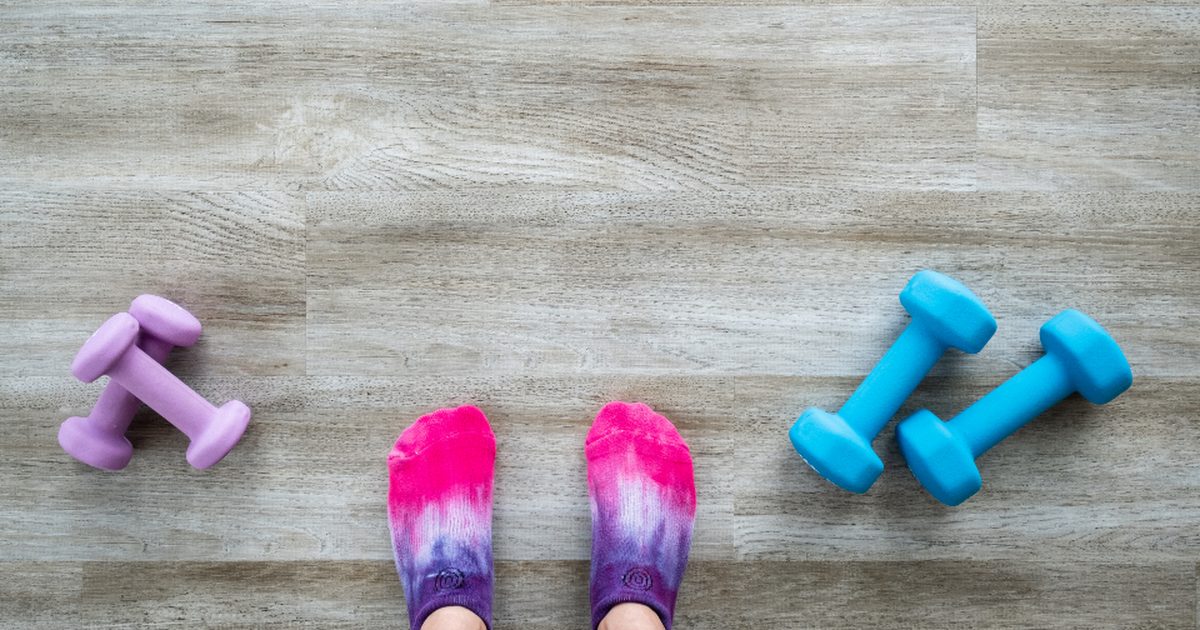 Pink socked feet on a wooden floor between pairs of lilac and aqua hand weights