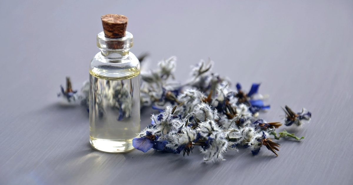 A small glass bottle of essential oil beside a scatter of dried blue flowers