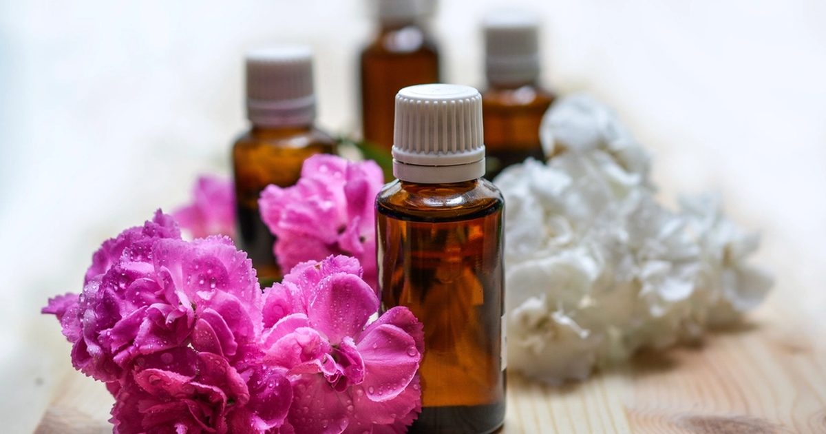 Amber glass essential oil bottles on a wooden table surrounded by pink and white flowers