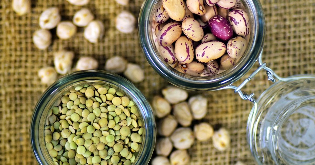 Glass jars of beans and lentils with chickpeas scattered on hessian