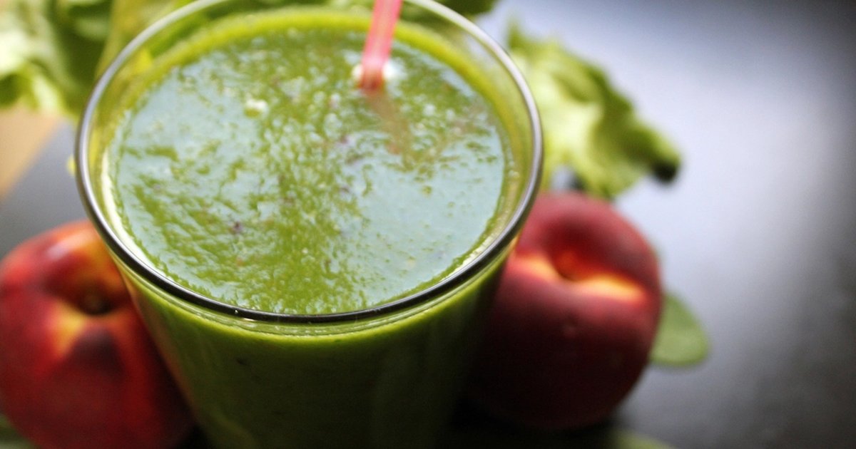 A tall glass of green smoothie next to two red apples