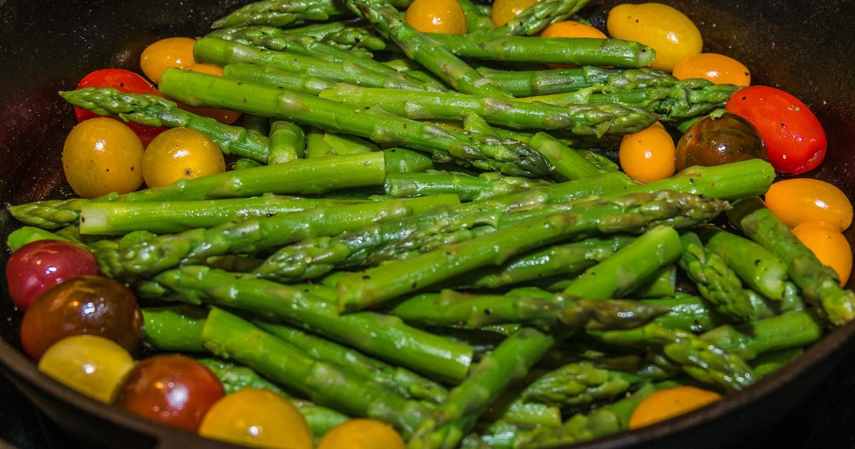 Asparagus and cherry tomatoes cooking in a cast iron pan