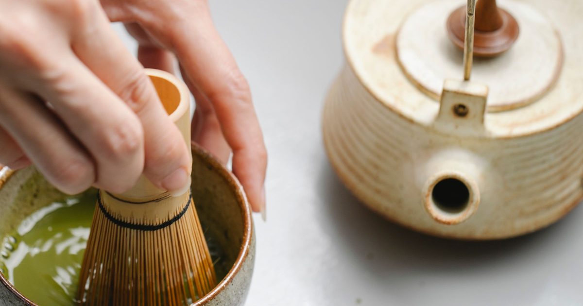 Whisking matcha in a ceramic bowl next to a stoneware teapot