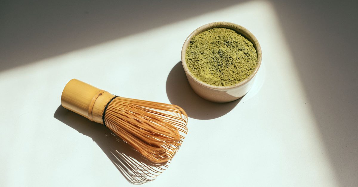 A bamboo whisk beside a small bowl of bright green matcha powder in soft morning light