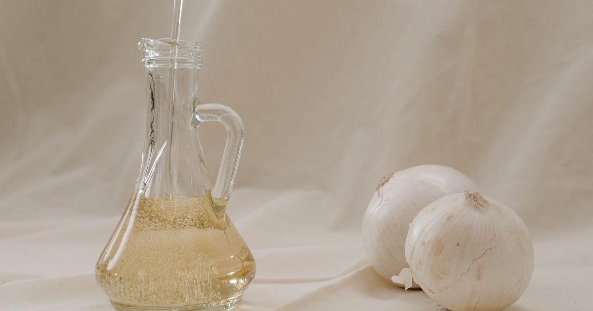 A glass jug of golden oil beside garlic bulbs on a linen cloth
