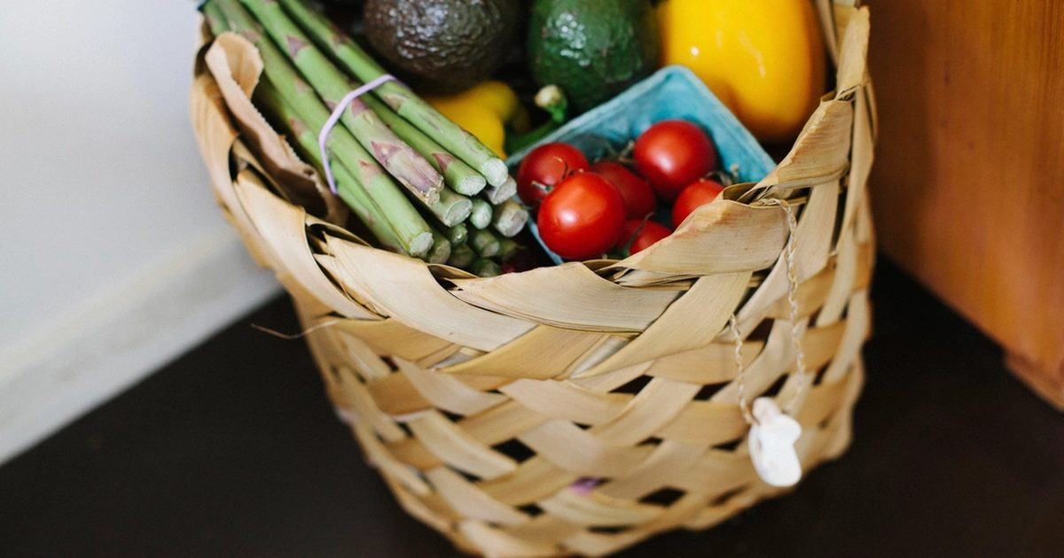 A woven basket of asparagus, avocados, tomatoes and capsicum