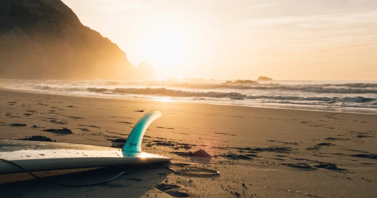 A surfboard on the sand at sunset