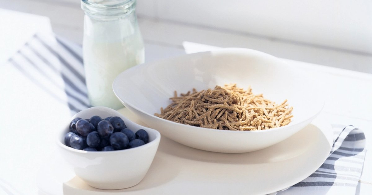 A glass bottle of milk beside a bowl of cereal and blueberries