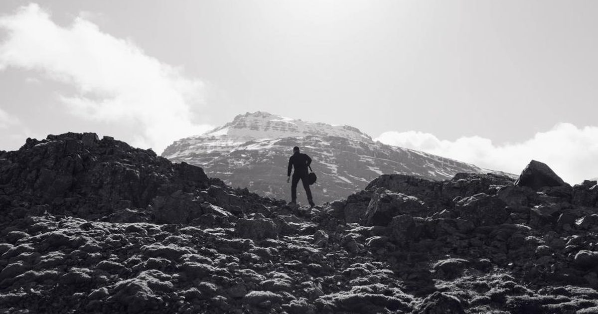 A lone hiker standing on dark volcanic rock beneath a pale mountain sky