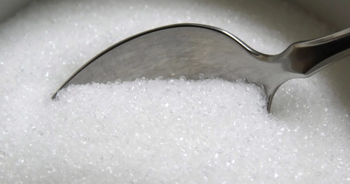 A metal spoon resting in a bowl of white sugar