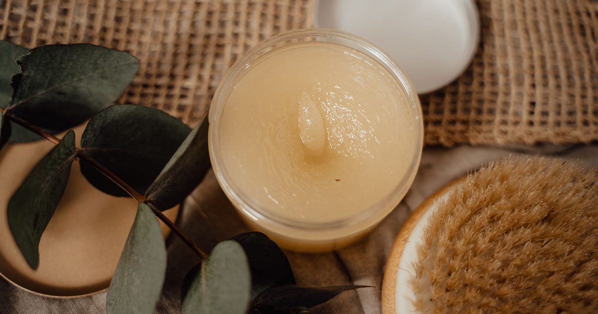 An open jar of pale tallow balm with eucalyptus leaves and a natural bristle brush