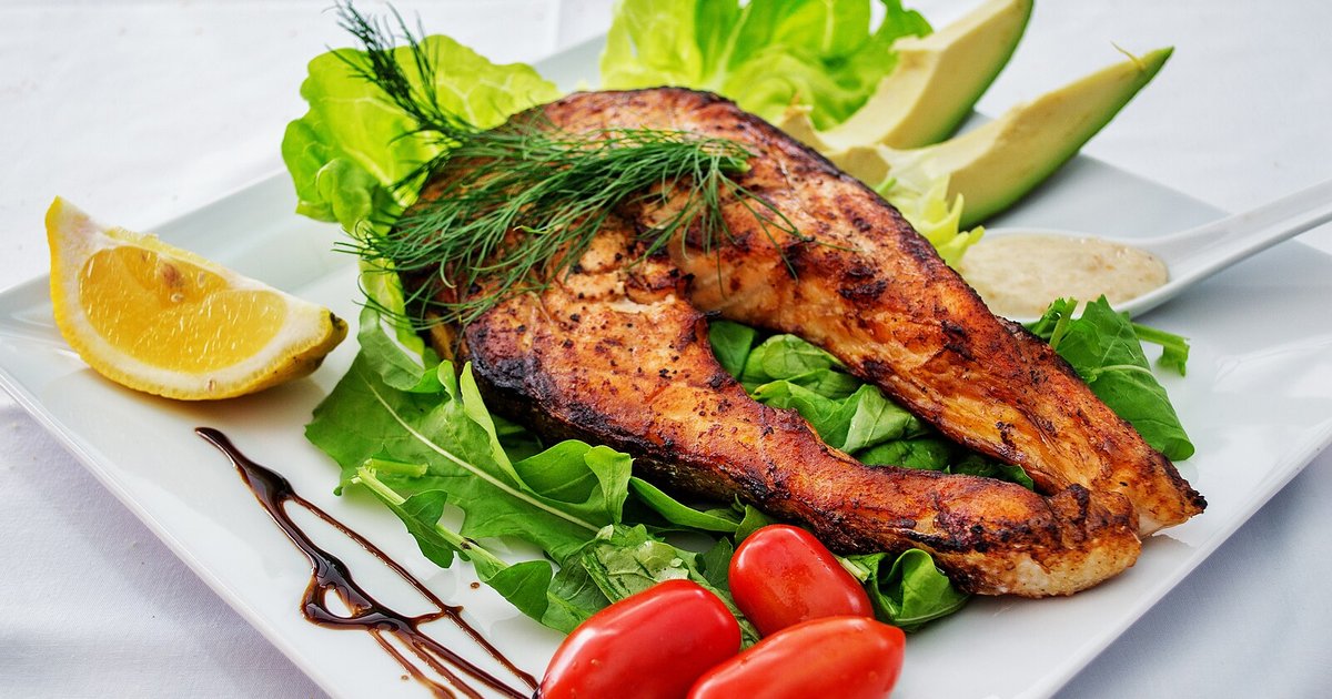 A grilled salmon steak served with salad, avocado and lemon